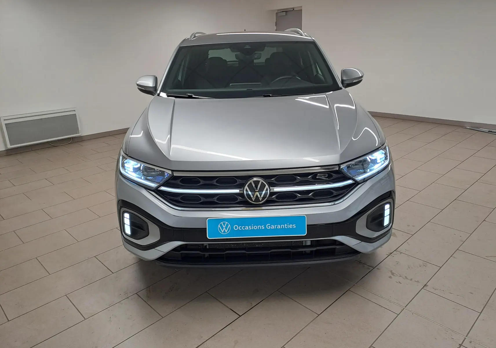 Vue frontale d’un Volkswagen T-Roc gris pyrite 2025 avec projecteurs Matrix LED allumés et calandre chromée.
