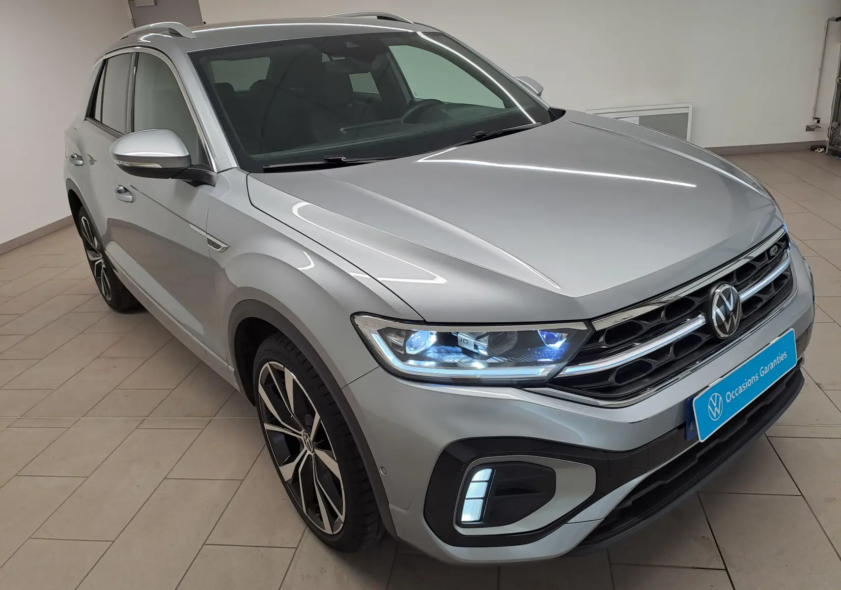 Volkswagen T-Roc gris pyrite en 3/4 avant droit, avec projecteurs Matrix LED allumés et jantes noires 19 pouces.