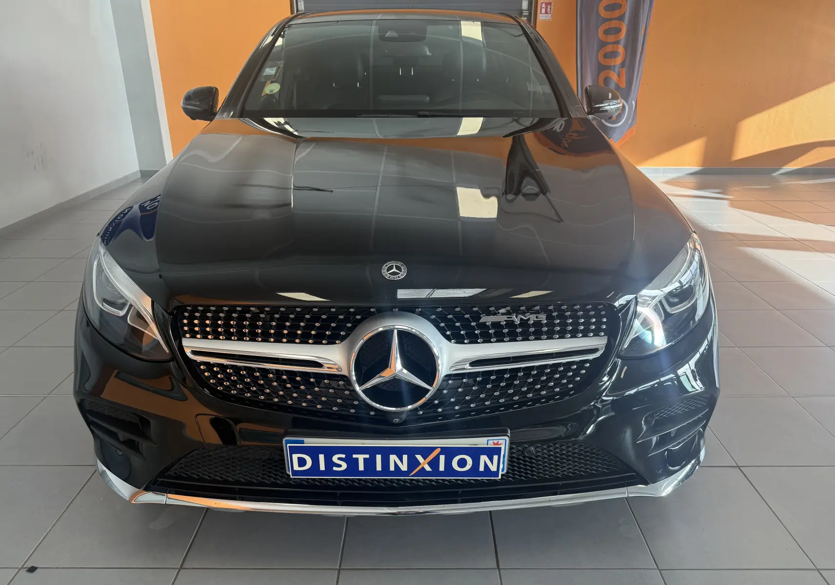 Vue frontale d'un Mercedes GLC Coupé noir 2018 avec calandre AMG et logo distinctif sur fond intérieur showroom.