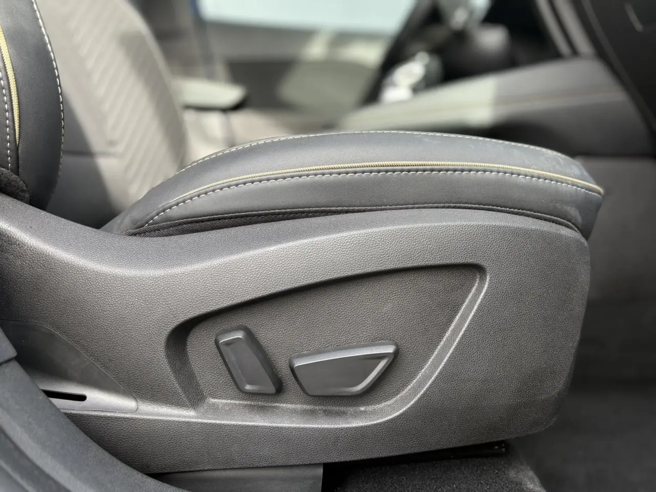 Gros plan sur les commandes de réglage électrique du siège avant du Renault Symbioz 2025, cuir noir avec surpiqûres jaunes.