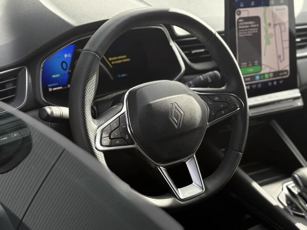 Gros plan sur le volant noir en cuir perforé du Renault Symbioz 2025 avec tableau de bord numérique et écran tactile GPS.