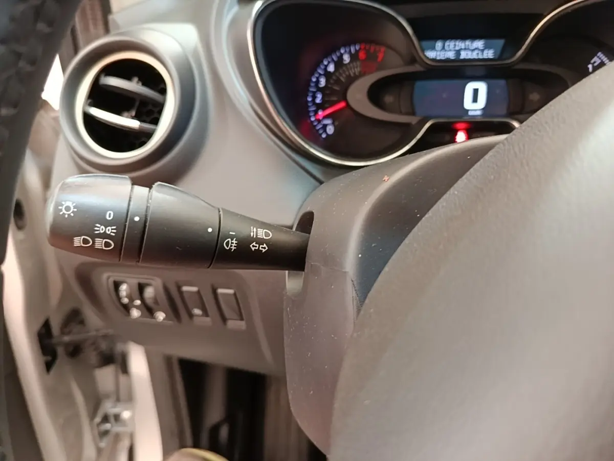 Vue rapprochée du tableau de bord et du commodo gauche du Renault Captur gris clair, affichage digital et commandes lumineuses visibles.