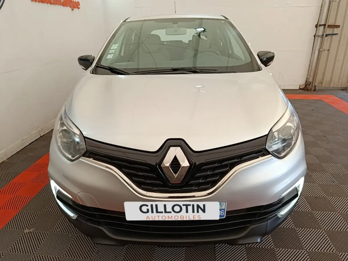 Vue frontale d'un Renault Captur gris clair 2018 avec feux de jour LED allumés dans un garage.