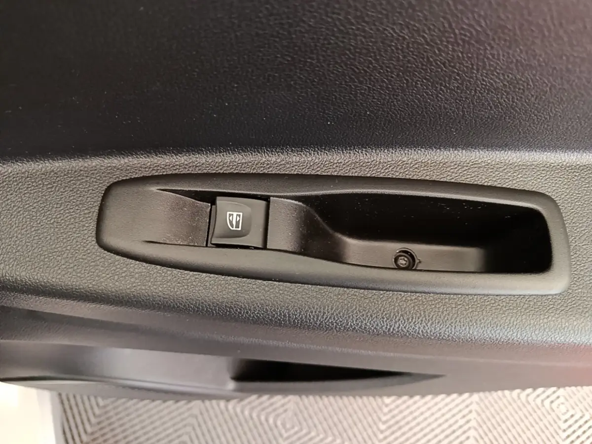 Gros plan sur le bouton de commande de lève-vitre noir intégré à la porte intérieure côté conducteur du Renault Captur gris clair.