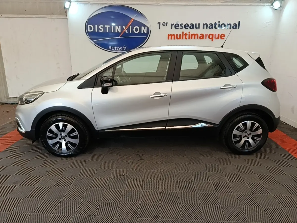 Profil droit d'un Renault Captur gris clair 2018 avec jantes alliage et rétroviseurs noirs, en intérieur showroom.