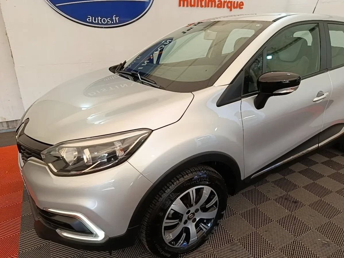 Renault Captur gris clair vu en 3/4 avant droit, avec feux à LED et rétroviseurs noirs brillants.