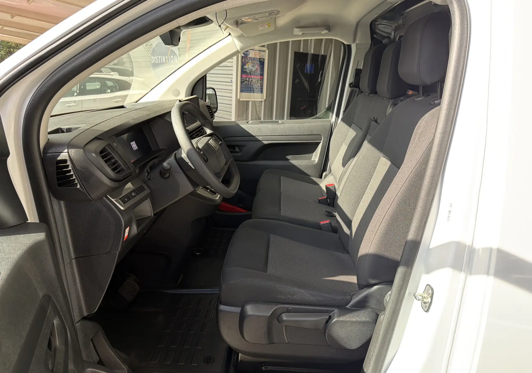 Vue intérieure côté conducteur du Fiat Scudo Fourgon blanc 2025, montrant la banquette modulable et le tableau de bord noir.