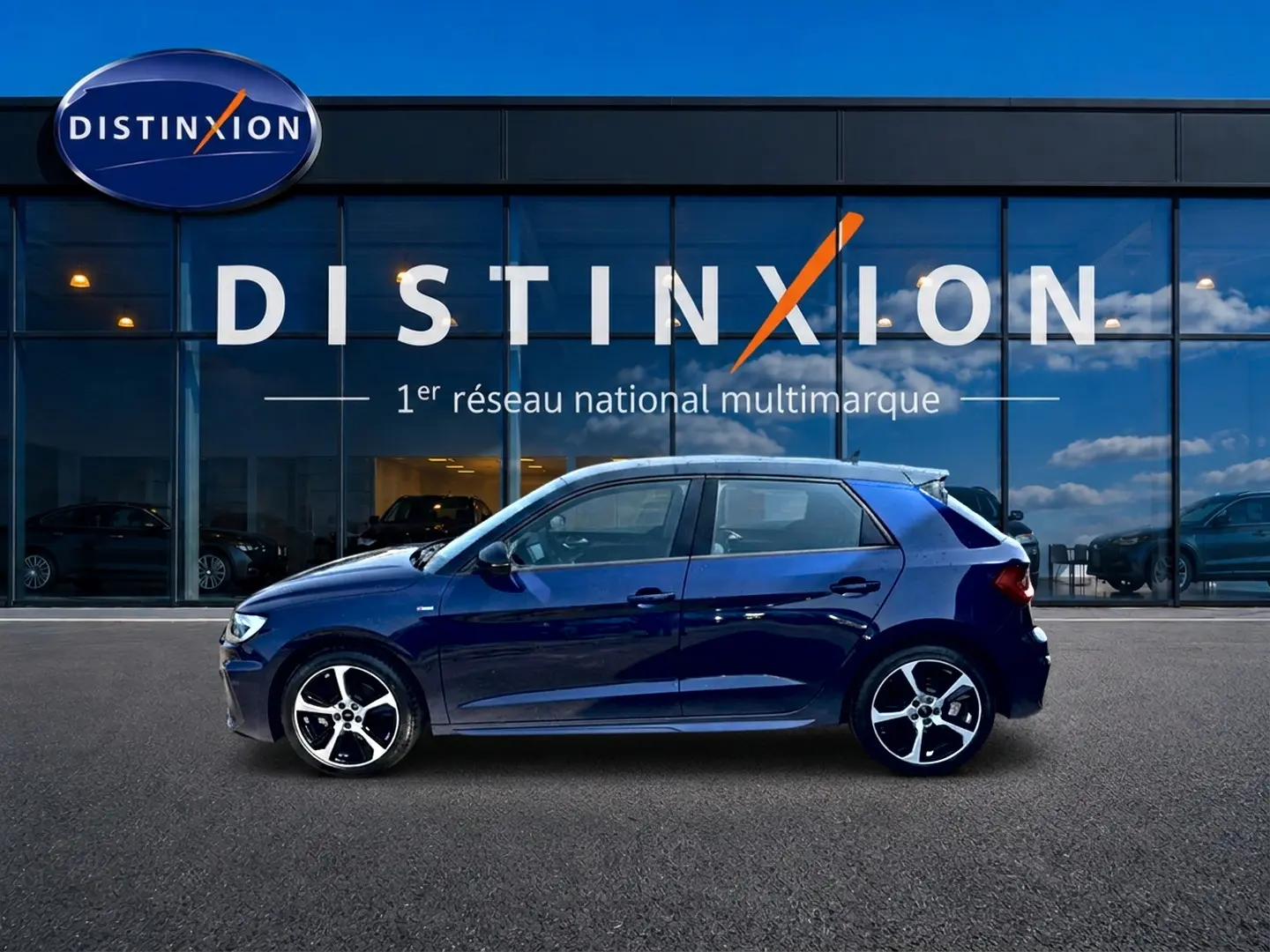 Profil côté gauche de l'Audi A1 Sportback 30 TFSI bleu foncé avec jantes alliage devant une vitrine Distinxion.