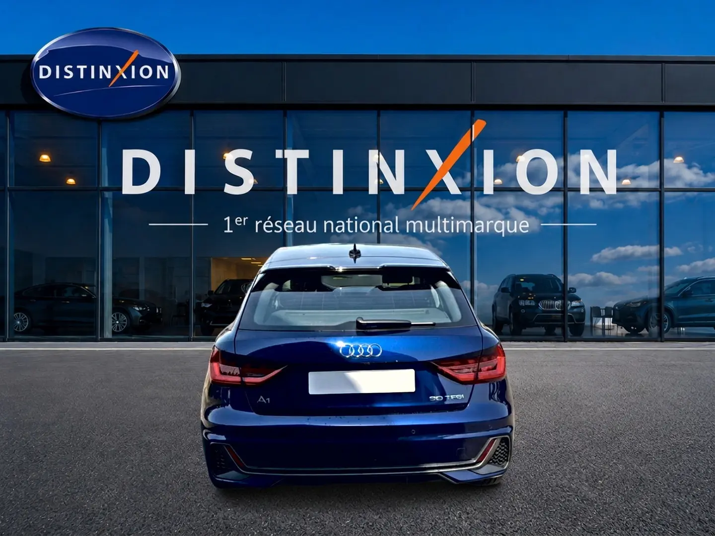 Vue arrière d'une Audi A1 Sportback 30 TFSI bleu foncé avec feux LED et becquet arrière, devant une vitrine Distinxion.