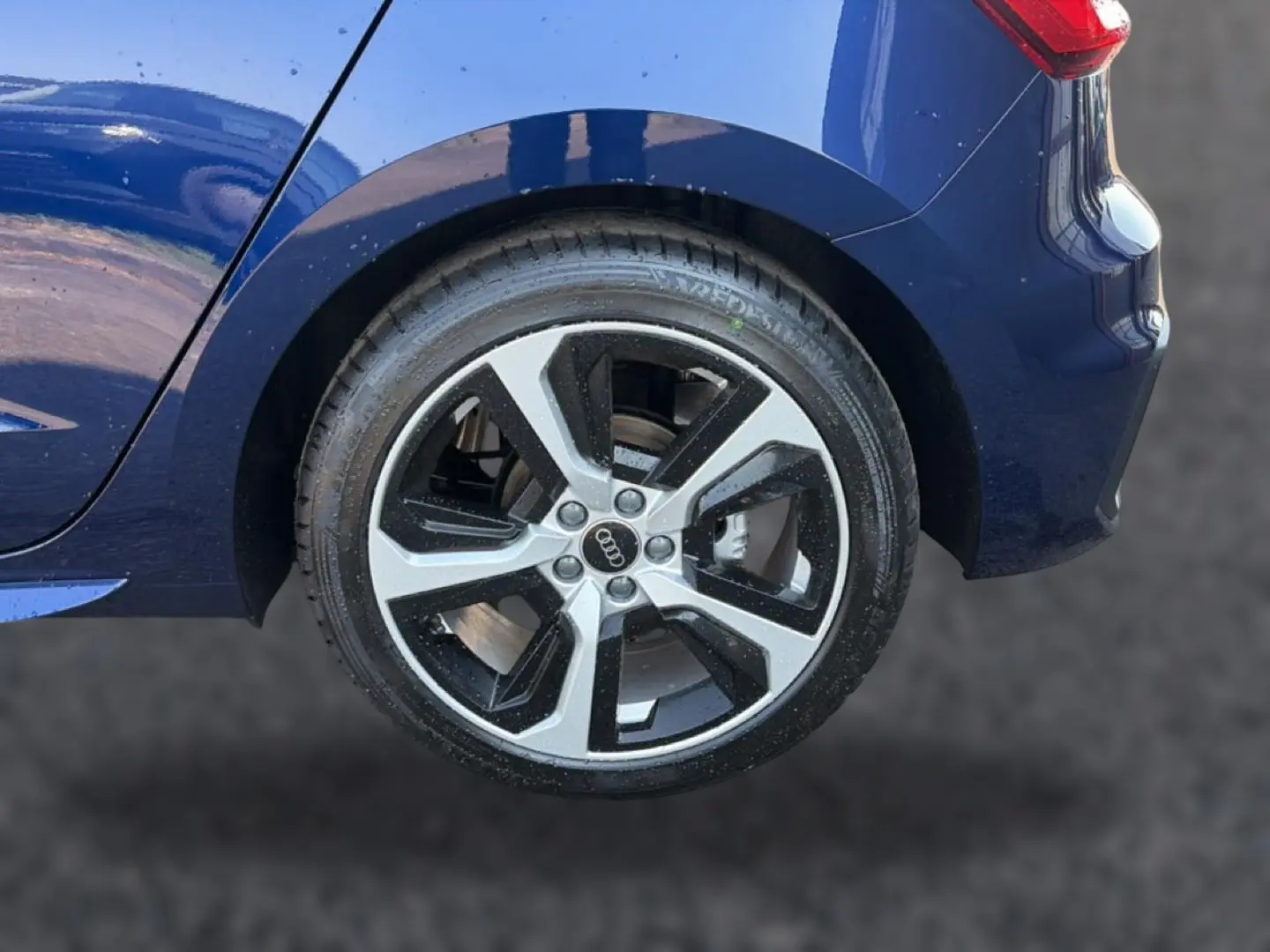 Gros plan sur la roue arrière droite d'une Audi A1 Sportback bleu foncé avec jante alu bicolore et feu arrière LED visible.