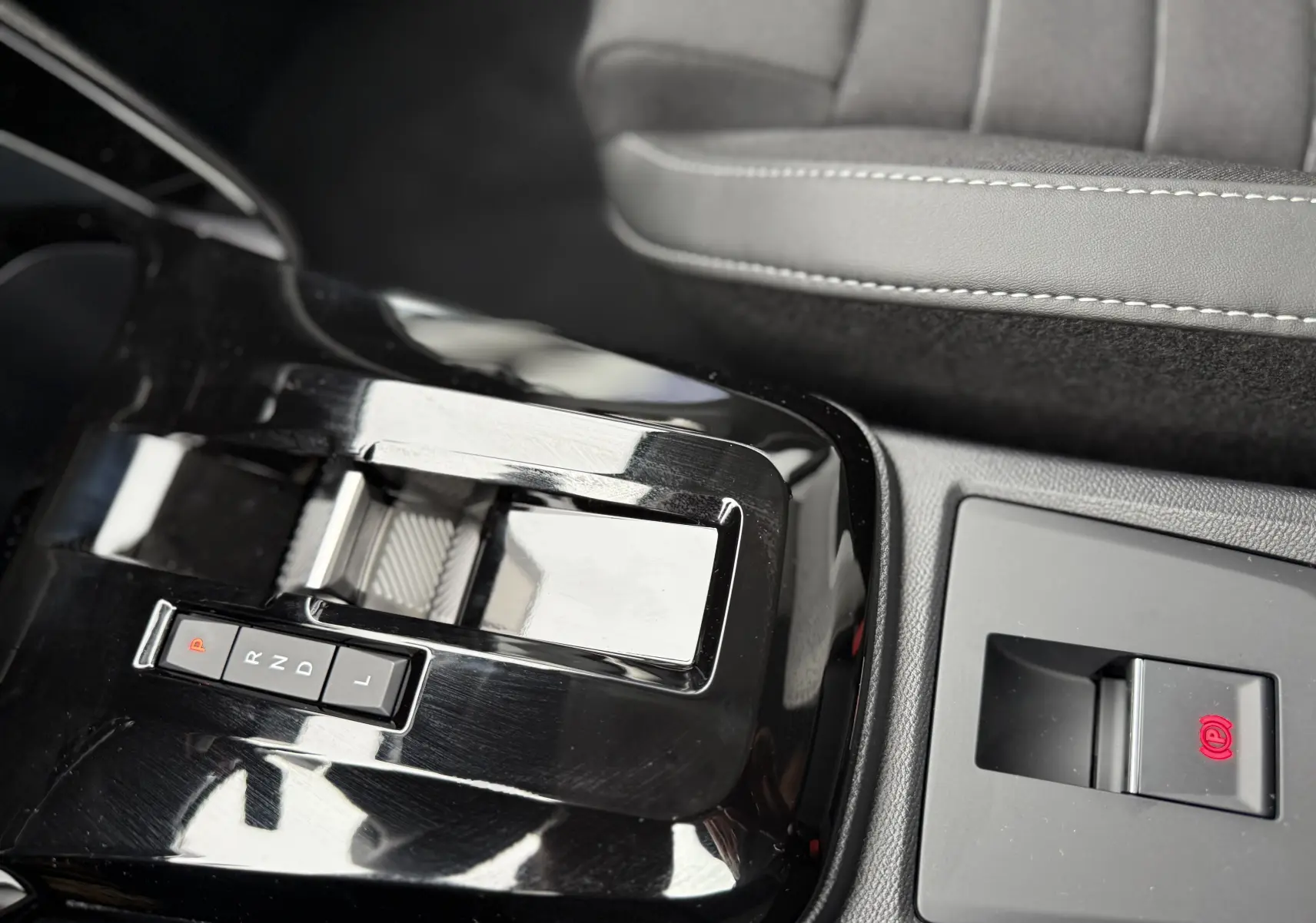 Gros plan sur la console centrale noire brillante de la Citroën C3 hybride 2026 avec levier de vitesses automatique et frein à main électrique.