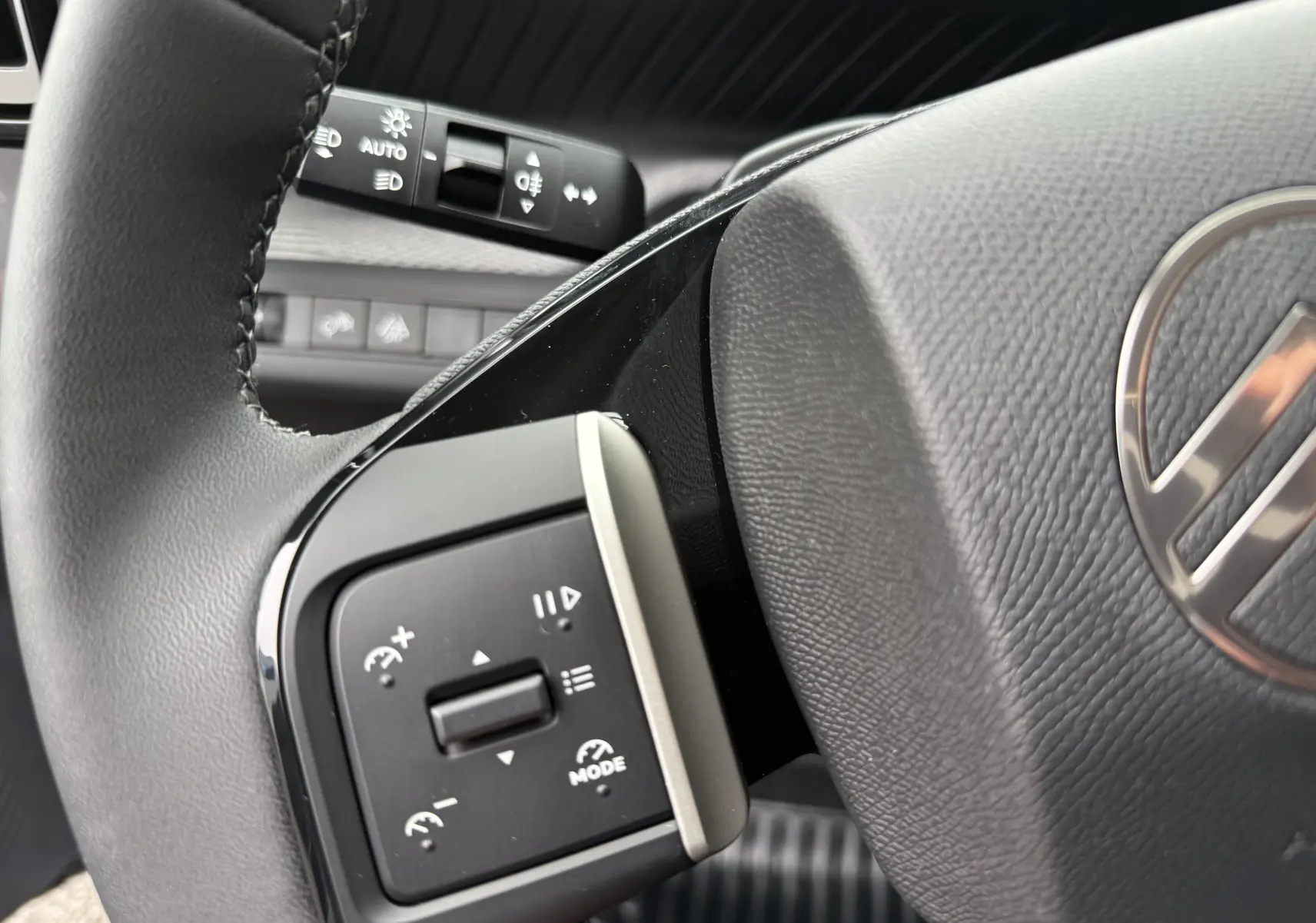 Gros plan sur les commandes au volant côté gauche du Citroën C3 hybride gris Mercury avec volant en cuir noir.