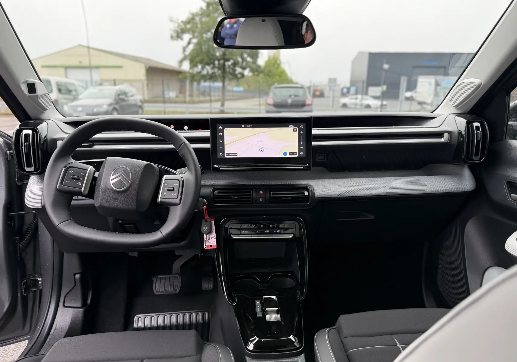 Vue intérieure avant de la Citroën C3 hybride 2026, tableau de bord noir avec écran tactile central et volant multifonction.