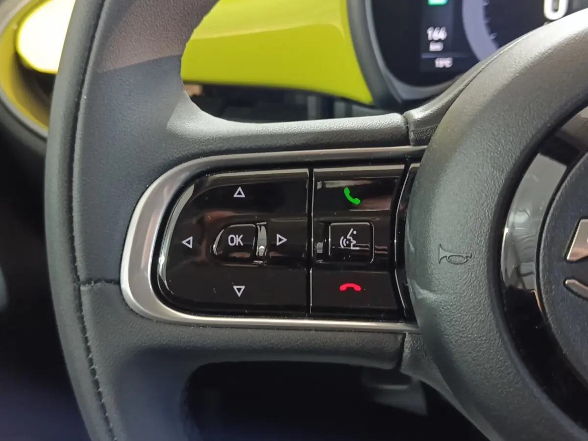 Gros plan sur le volant cuir synthétique noir du Fiat 500 BEV 24KWH 2024 avec commandes multifonctions et tableau de bord jaune visible.