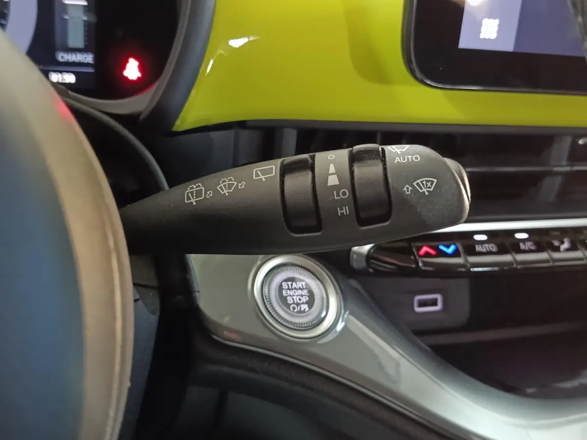 Gros plan sur la commande d’essuie-glace et le bouton start/stop dans l’habitacle jaune vif d’une Fiat 500 électrique 2024.