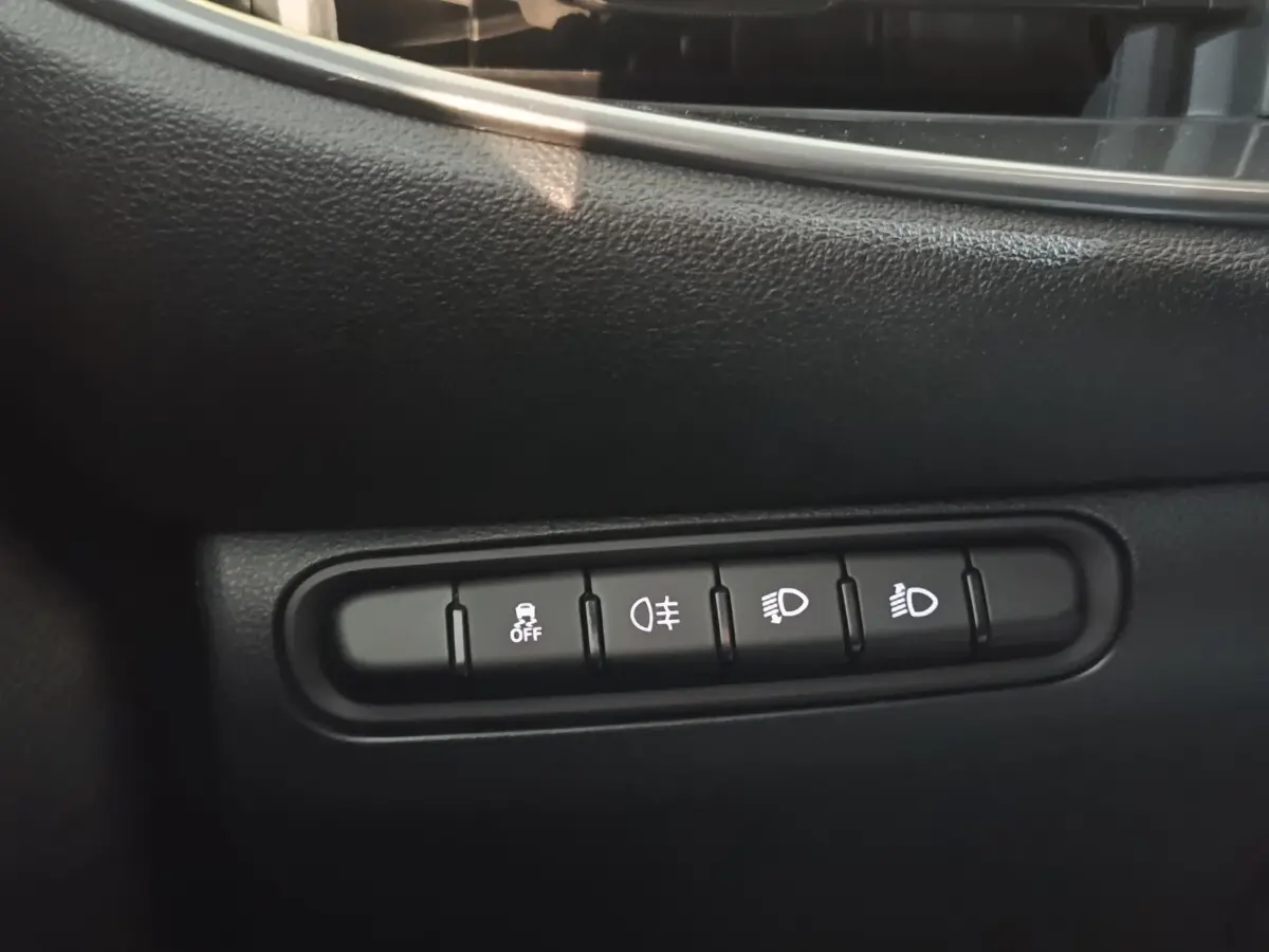 Gros plan sur les boutons de commande des phares et de l'antipatinage dans l'habitacle noir du Fiat 500 BEV 24KWH jaune.