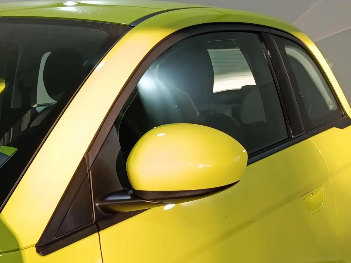 Gros plan sur le rétroviseur côté gauche d'une FIAT 500 BEV 24KWH jaune électrique, avec vitre arrière visible.