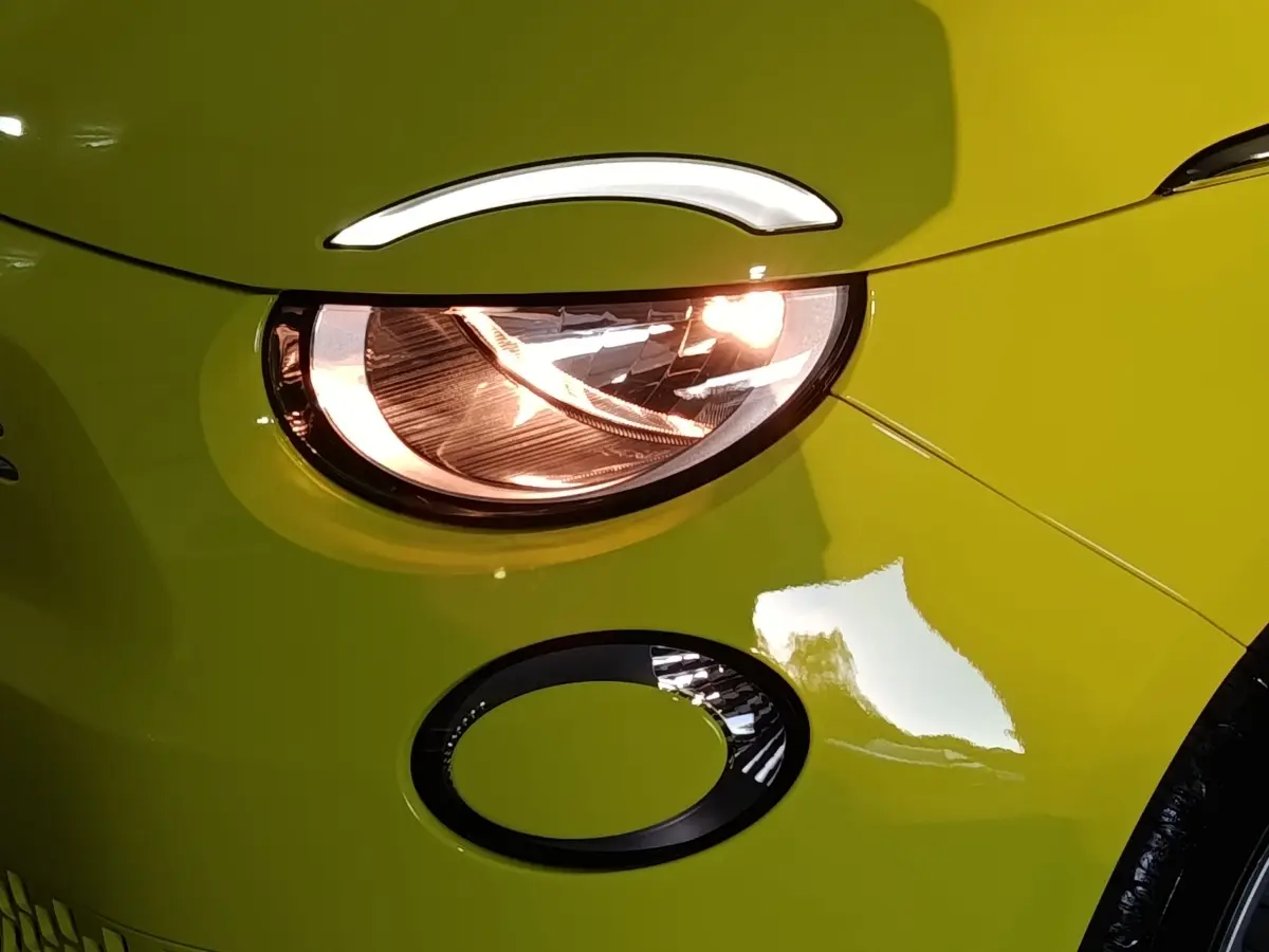 Gros plan sur le phare avant droit allumé d'une FIAT 500 BEV 24KWH jaune vif avec détail du clignotant rond noir.