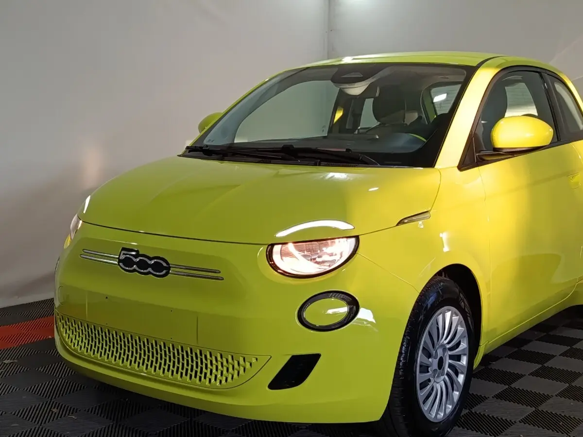 Vue 3/4 avant droite d'une FIAT 500 BEV 24KWH jaune électrique avec phares allumés et jantes argentées.