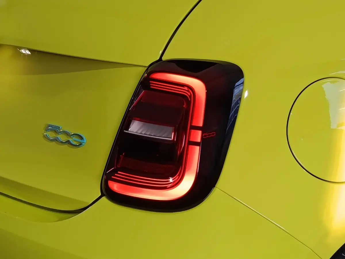 Gros plan sur le feu arrière droit rouge et le logo 500e bleu d'une FIAT 500 électrique jaune vif.