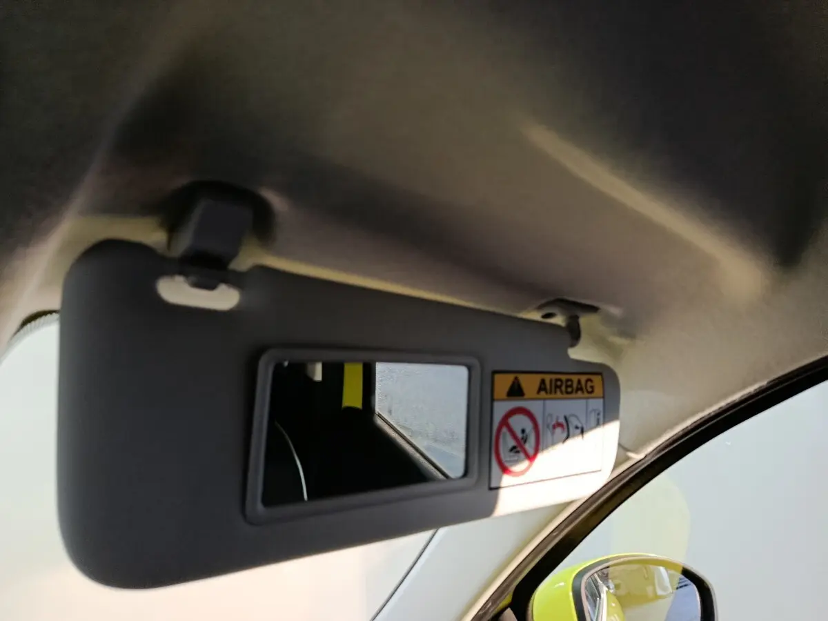 Détail du pare-soleil côté conducteur avec miroir intégré, reflet du rétroviseur et carrosserie jaune vif visible.
