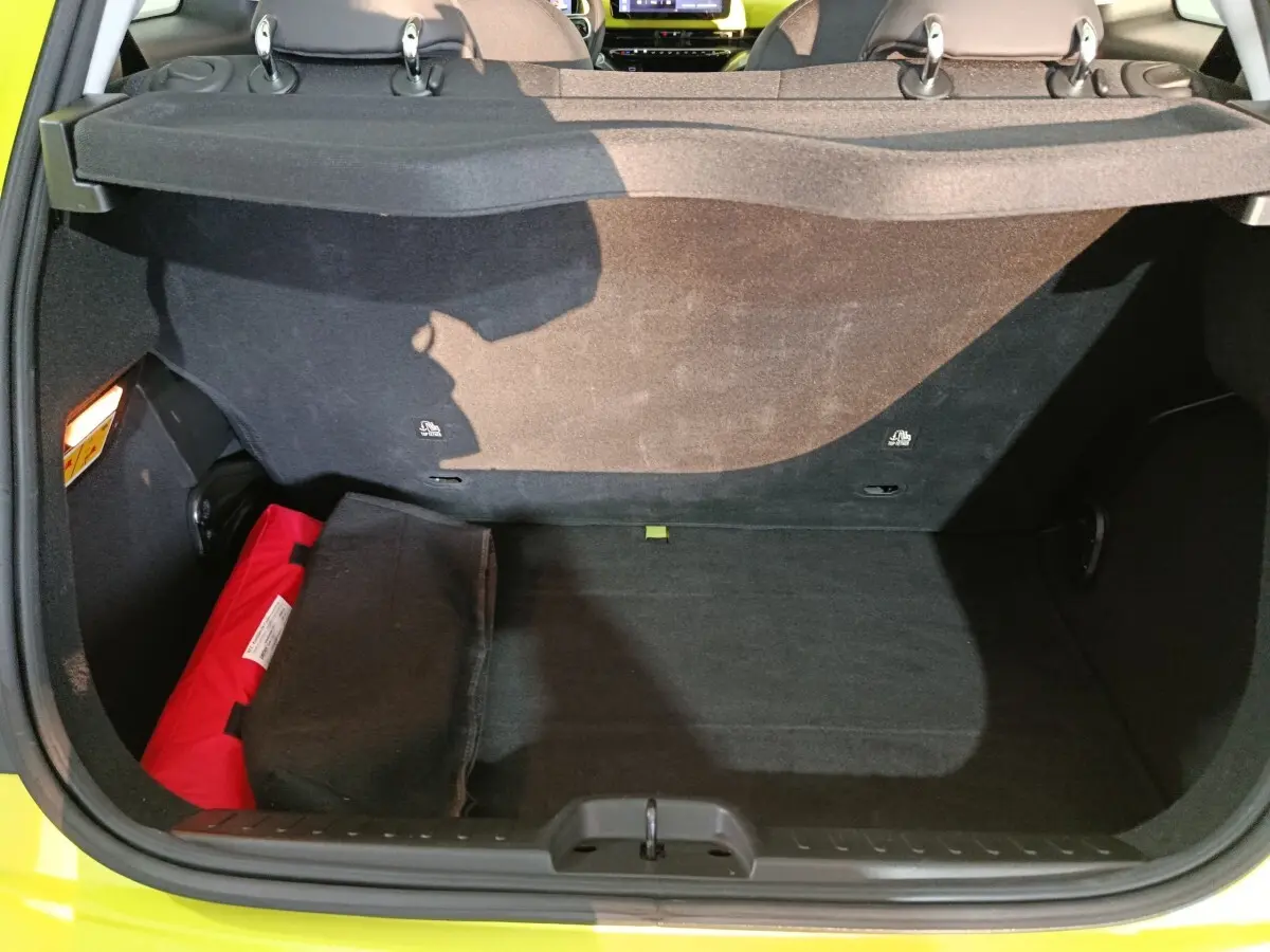 Coffre ouvert vu de l'arrière d'une FIAT 500 BEV 24KWH jaune, avec banquette arrière et trousse de secours rouge visible.