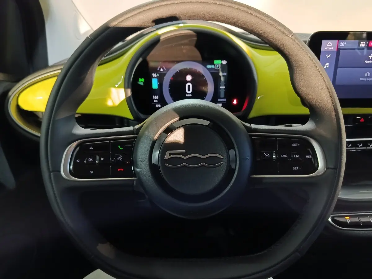 Vue rapprochée du volant cuir synthétique noir du Fiat 500 BEV 24KWH 2024 avec tableau de bord jaune et écran numérique.