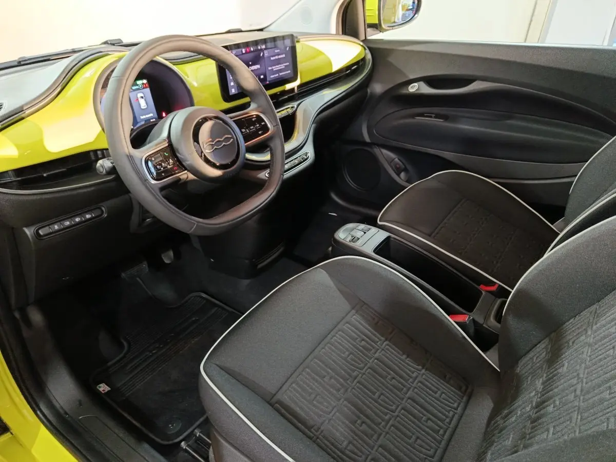 Vue intérieure côté conducteur de la Fiat 500 BEV 24KWH 2024 avec tableau de bord jaune et volant multifonctions cuir synthétique.