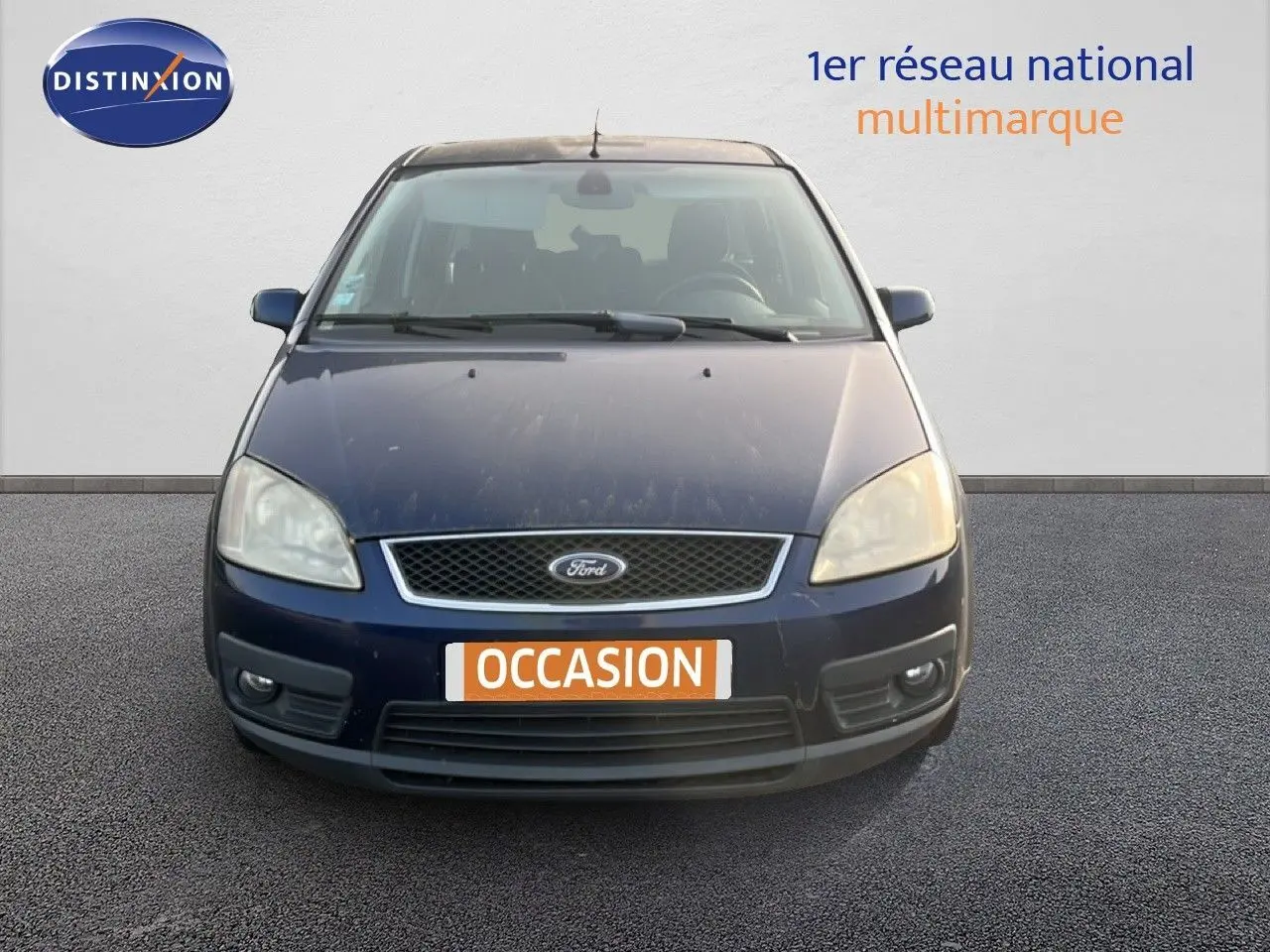 Vue frontale d'une Ford C-MAX 2005 bleu foncé métal avec plaque "OCCASION" et phares légèrement ternis.