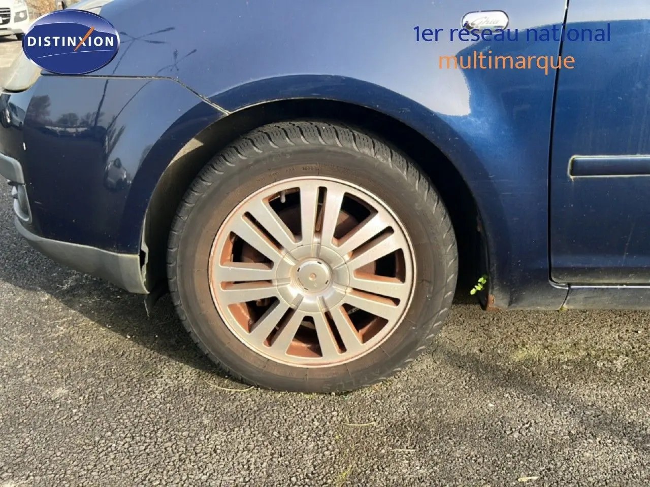 Gros plan sur la roue avant gauche d'une Ford C-MAX bleu foncé métal de 2005, avec jante en alliage et carrosserie légèrement usée.