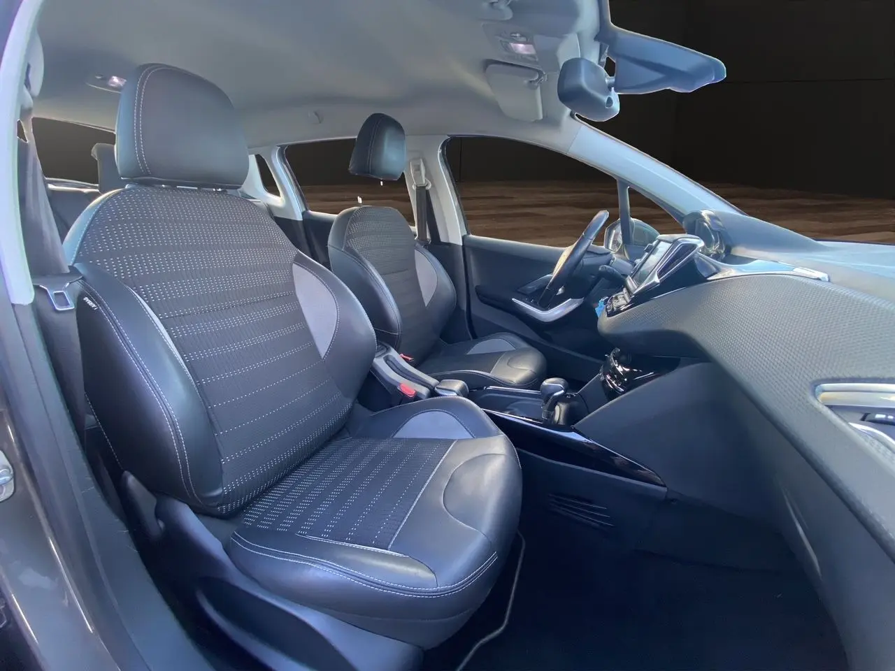 Vue intérieure côté conducteur du Peugeot 2008 gris platinium, mettant en valeur les sièges tissu et cuir avec surpiqûres blanches.