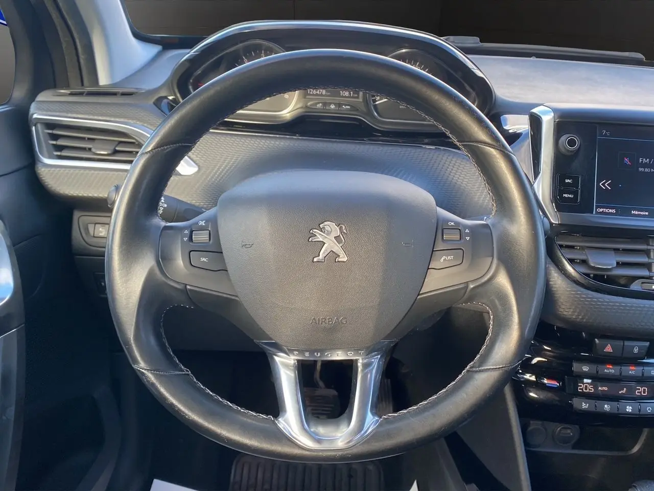 Vue intérieure centrée sur le volant cuir noir du Peugeot 2008 gris platinium avec tableau de bord et écran tactile.