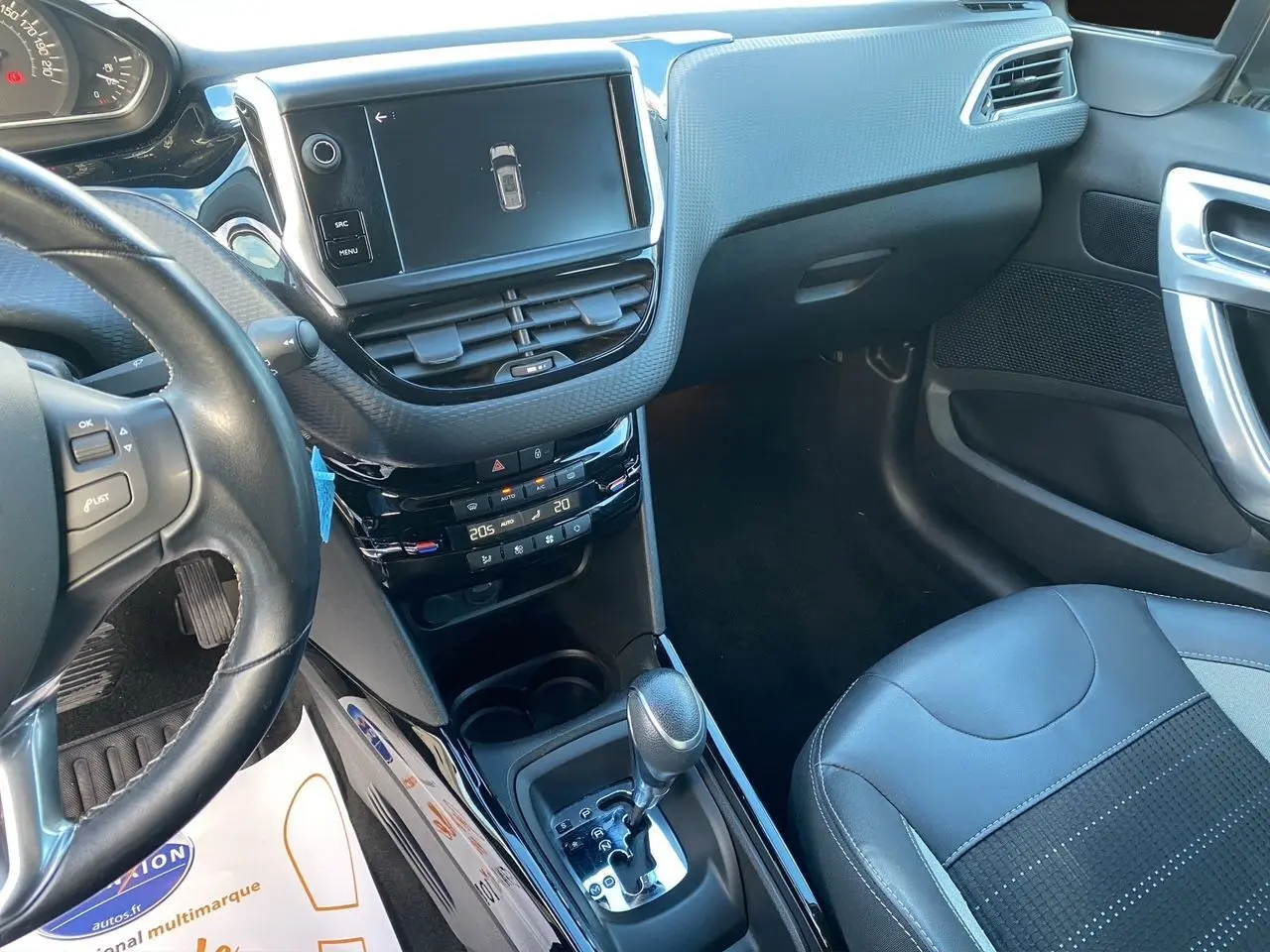 Vue intérieure côté conducteur du tableau de bord et console centrale noire du Peugeot 2008 gris platinium avec écran tactile et boîte automatique.