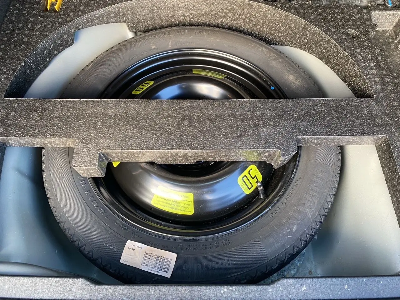 Roue de secours noire avec étiquette jaune, logée dans le coffre d’un Peugeot 2008 gris platinium de 2019.