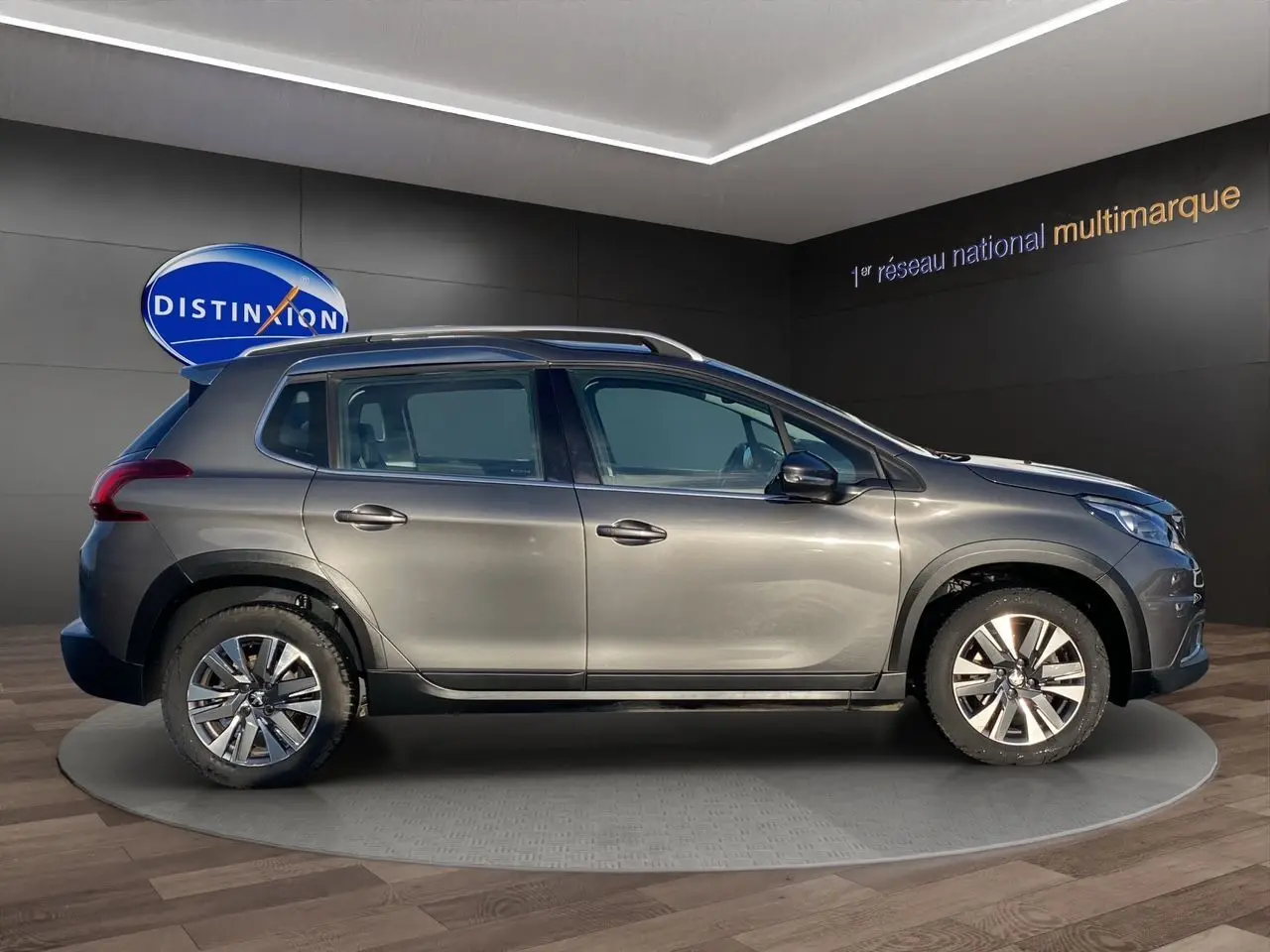 Peugeot 2008 gris platinium vue de profil côté gauche, avec jantes alliage et barres de toit visibles.