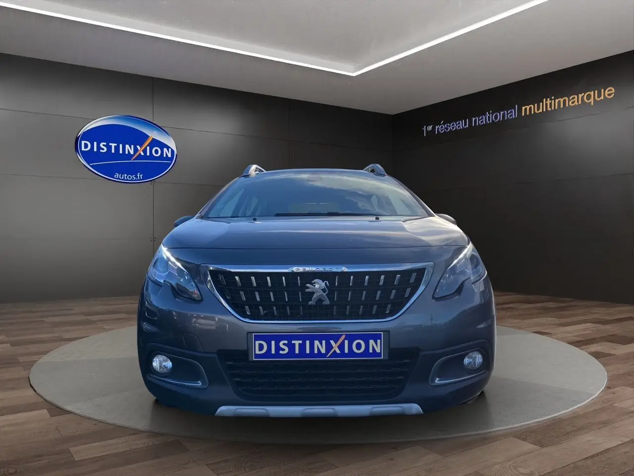 Vue frontale d'un Peugeot 2008 gris platinium avec calandre distinctive et phares allumés en showroom.