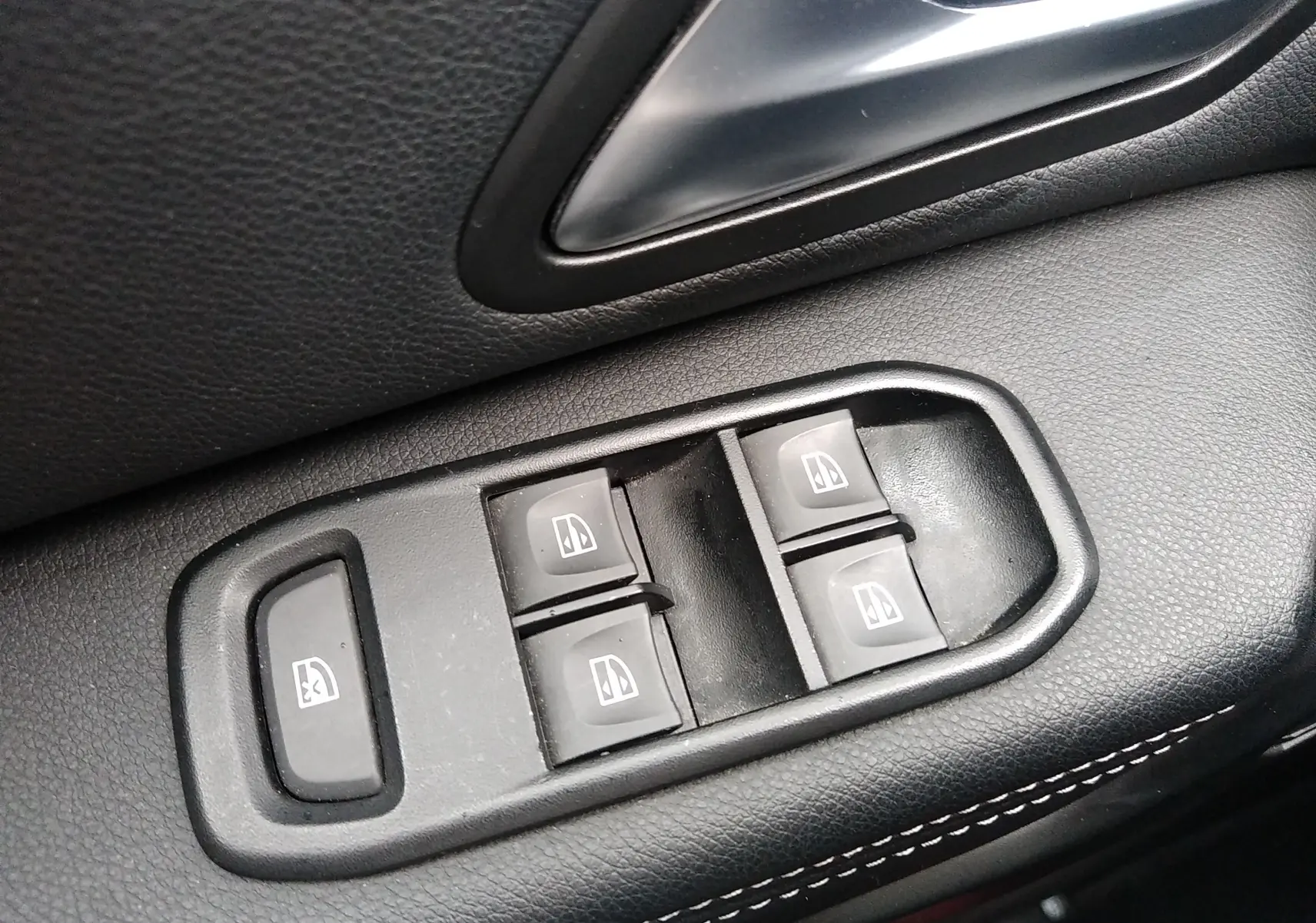 Gros plan sur les commandes de lève-vitres électriques côté conducteur du Dacia Duster 2021, intérieur noir avec surpiqûres blanches.
