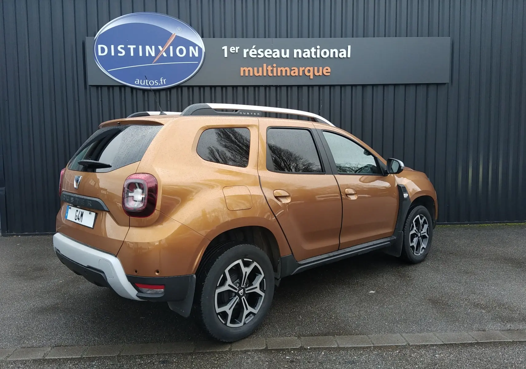 Vue 3/4 arrière droite du Dacia Duster 2021 orange Atacama avec jantes alliage et barres de toit argentées.