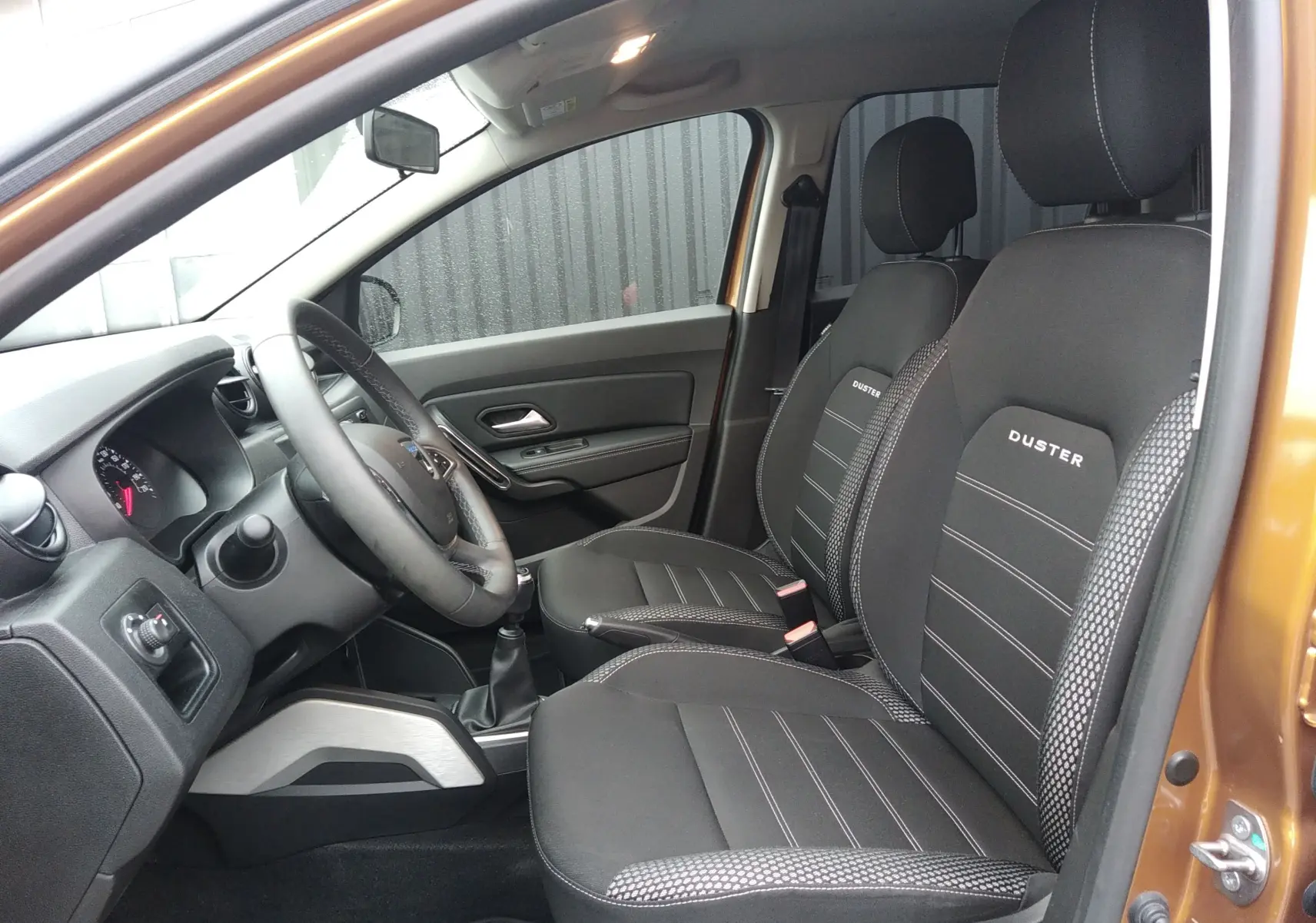 Vue intérieure côté conducteur du Dacia Duster 2021 orange Atacama, sièges noirs avec logo Duster brodé.