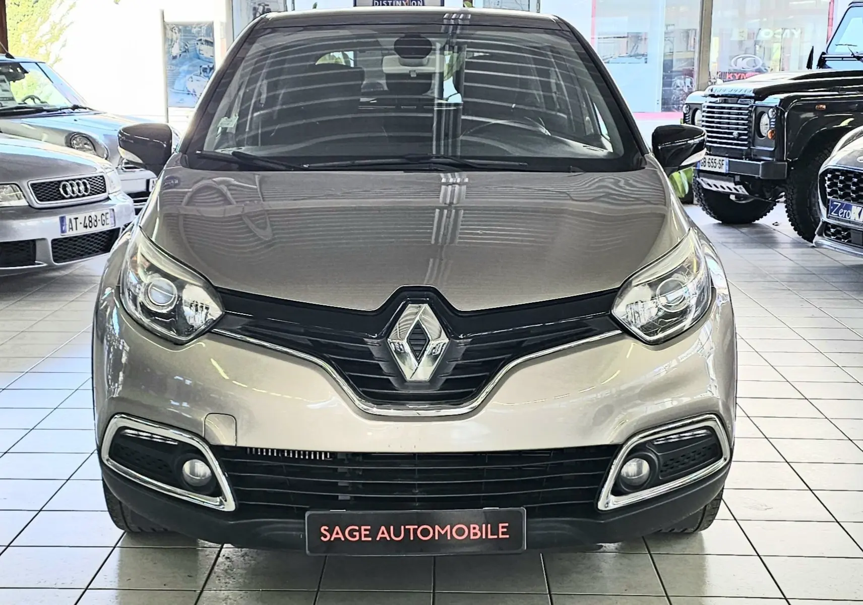 Vue frontale d'un Renault Captur gris 2014 en showroom, mettant en valeur la calandre et les phares distinctifs.