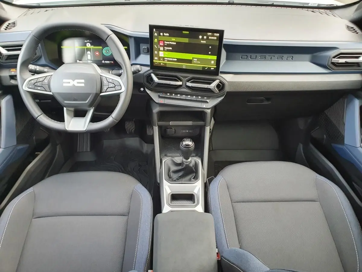 Vue intérieure avant du Dacia Duster 2025 avec tableau de bord moderne, écran tactile, volant multifonction et boîte manuelle.