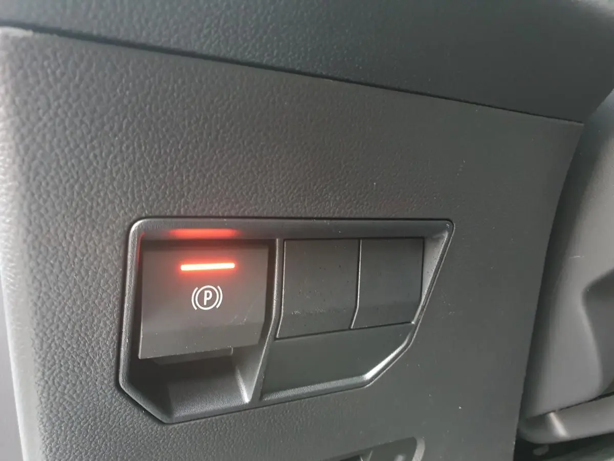 Gros plan sur le bouton de frein à main électrique allumé dans l'habitacle noir du Dacia Duster blanc Glacier.