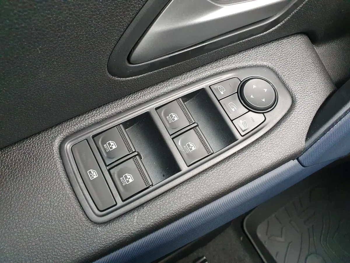 Gros plan sur les commandes de lève-vitres et rétroviseurs côté conducteur du Dacia Duster 2025, intérieur noir et bleu.