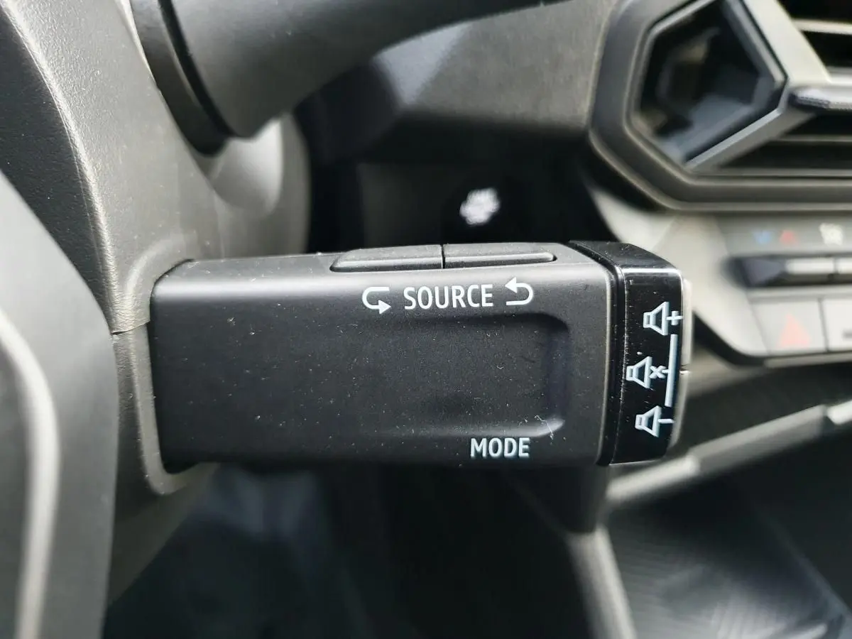 Gros plan sur la commande multimédia noire à gauche du volant du Dacia Duster 2025, intérieur gris et noir.