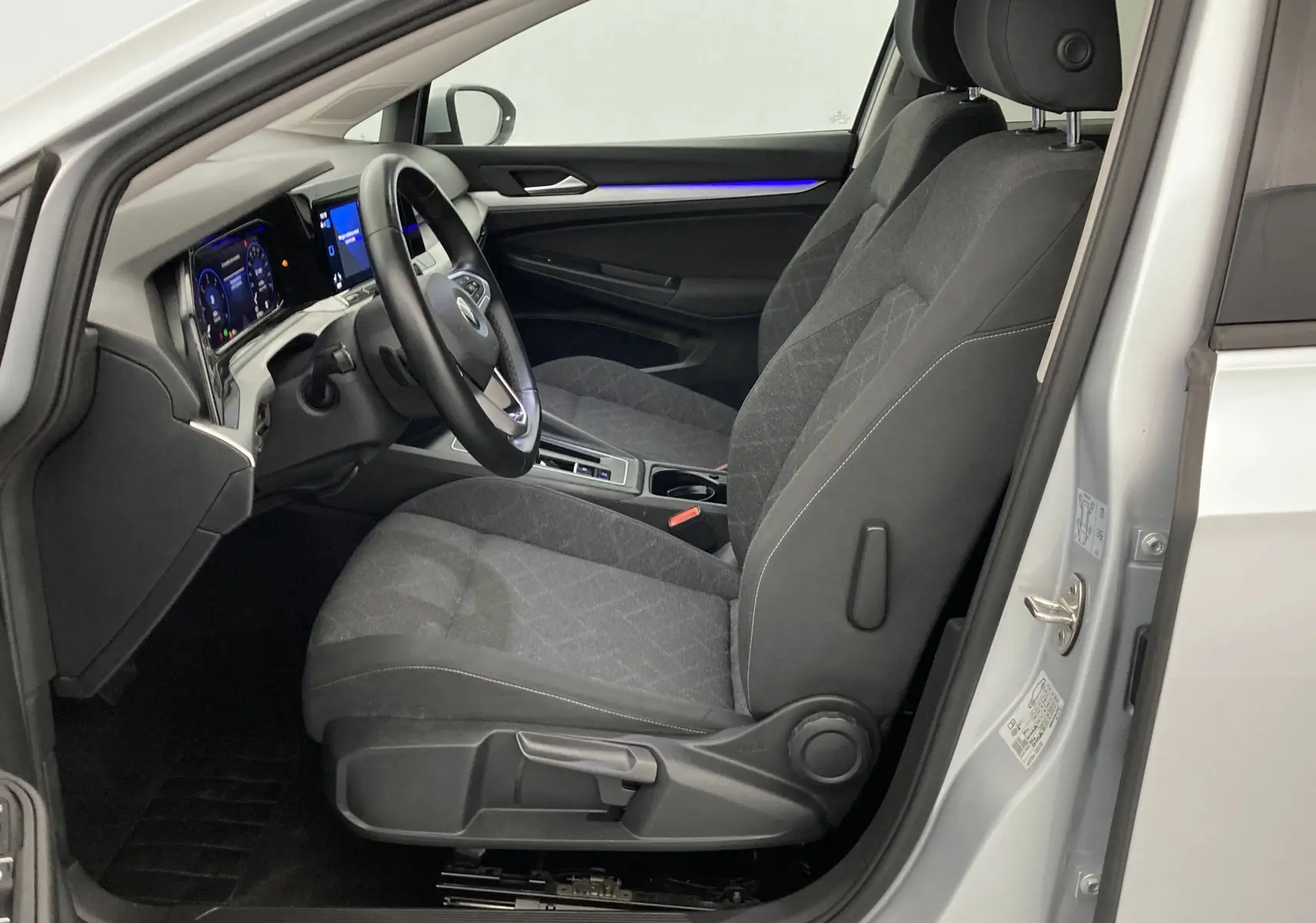 Intérieur côté conducteur de la Volkswagen Golf VIII gris reflex, montrant sièges tissu et tableau de bord digital.