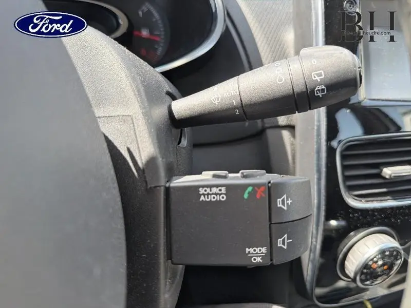 Commande audio au volant et manette d'essuie-glace dans un intérieur de voiture, avec logo Ford visible.