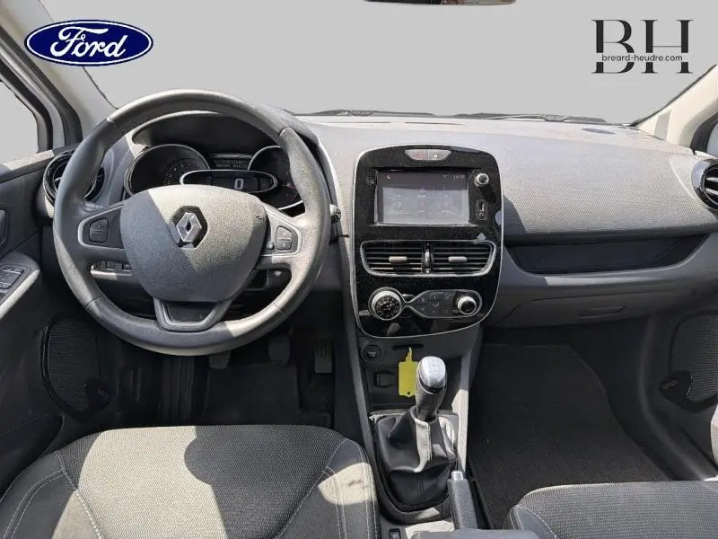 Vue intérieure avant de la Renault Clio blanche de 2018, montrant le volant cuir, tableau de bord et levier de vitesse manuel.