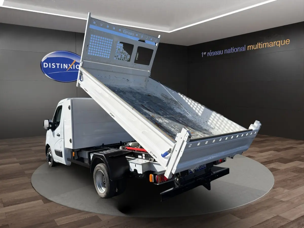 Renault Master blanc en 3/4 arrière avec benne basculante relevée, sur fond intérieur showroom.