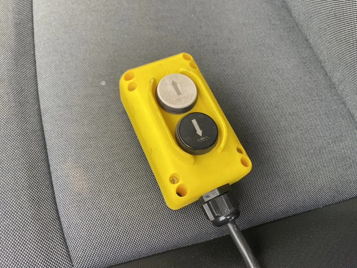 Télécommande jaune avec deux boutons fléchés, posée sur un siège gris à l'intérieur du Renault Master blanc.