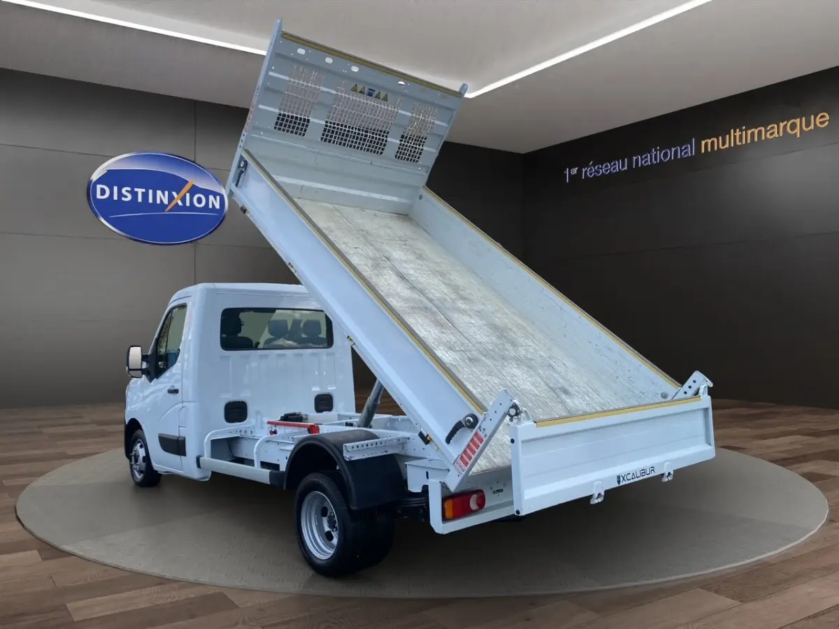Vue 3/4 arrière d’un Renault Master blanc 2024 avec benne basculante relevée dans un showroom.